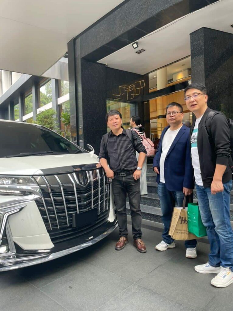Three guests with shopping bags standing beside a white luxury MPV at a hotel entrance