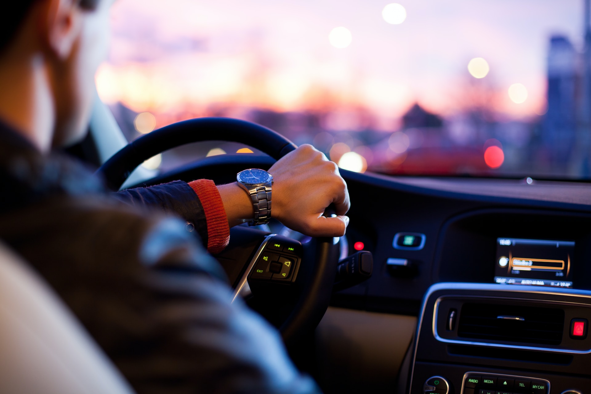 A chauffeur's hand on the steering wheel at dusk
