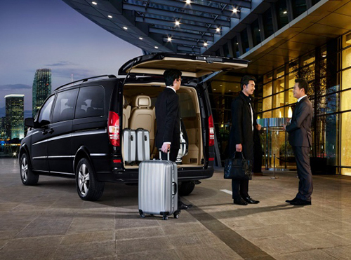 Chauffeurs in suits loading luggage into a black van outside a hotel lobby